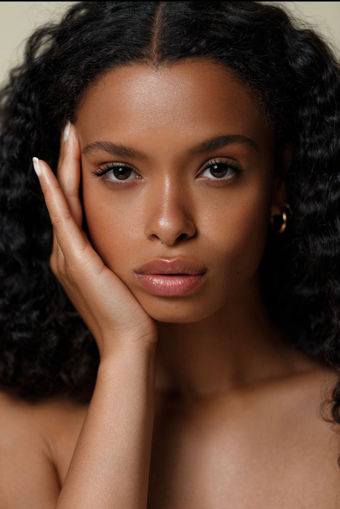 Woman with dark curly hair resting her head on her hand against a neutral background